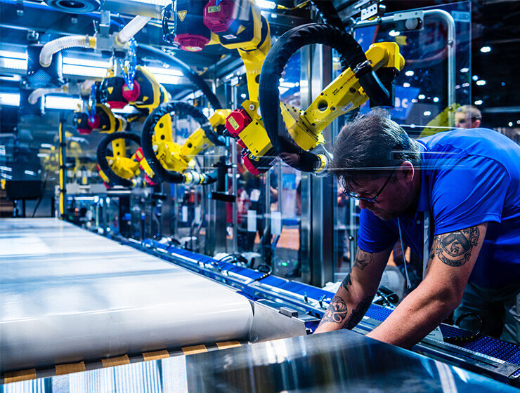 A Delkor service technician is shown working on a Delkor machine with yellow robotic arms in the background.