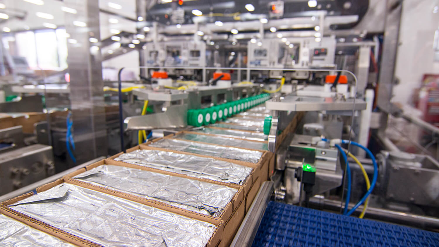 Many corrugate boxes with cheese blocks are shown on the conveyor coming out of Delkor's L Series Lidder