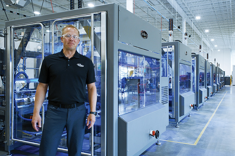 Delkor's VP of Engineering, Rick Gessler, stands in front of a line of Trayfecta machines