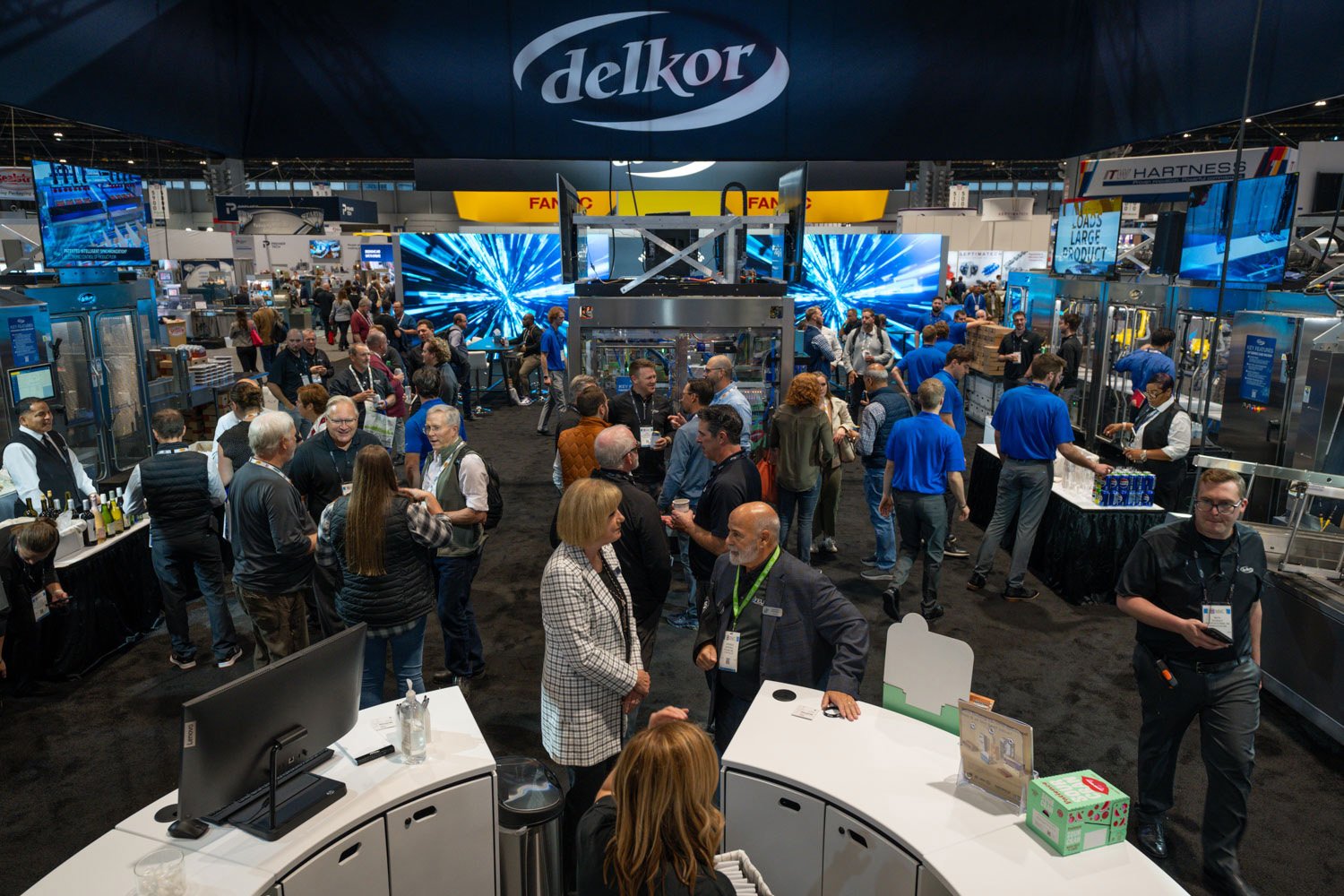 An image of a tradeshow booth with a large Delkor sign on top and lots of people surrounding equipment An image of a tradeshow booth with a large Delkor sign on top and lots of people surrounding equipment